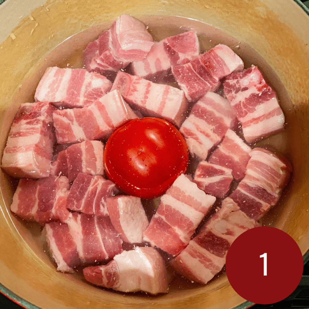 cut up pork belly with a red tomato in a pot filled with water